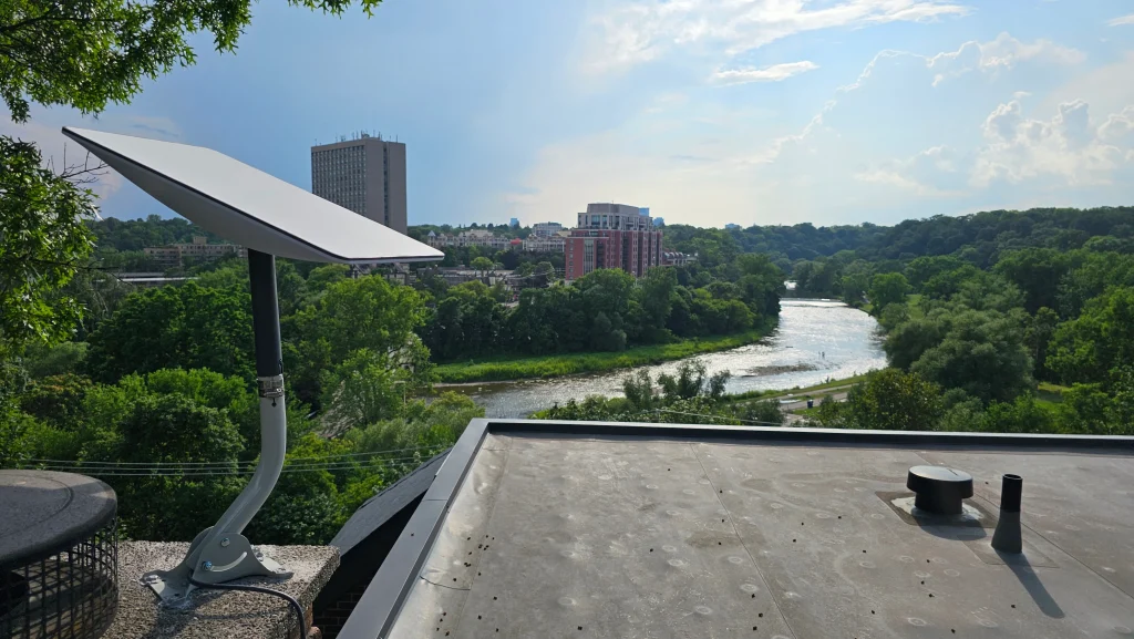 A Starlink satellite dish mounted on a brick chimney, overlooking a river and city skyline.