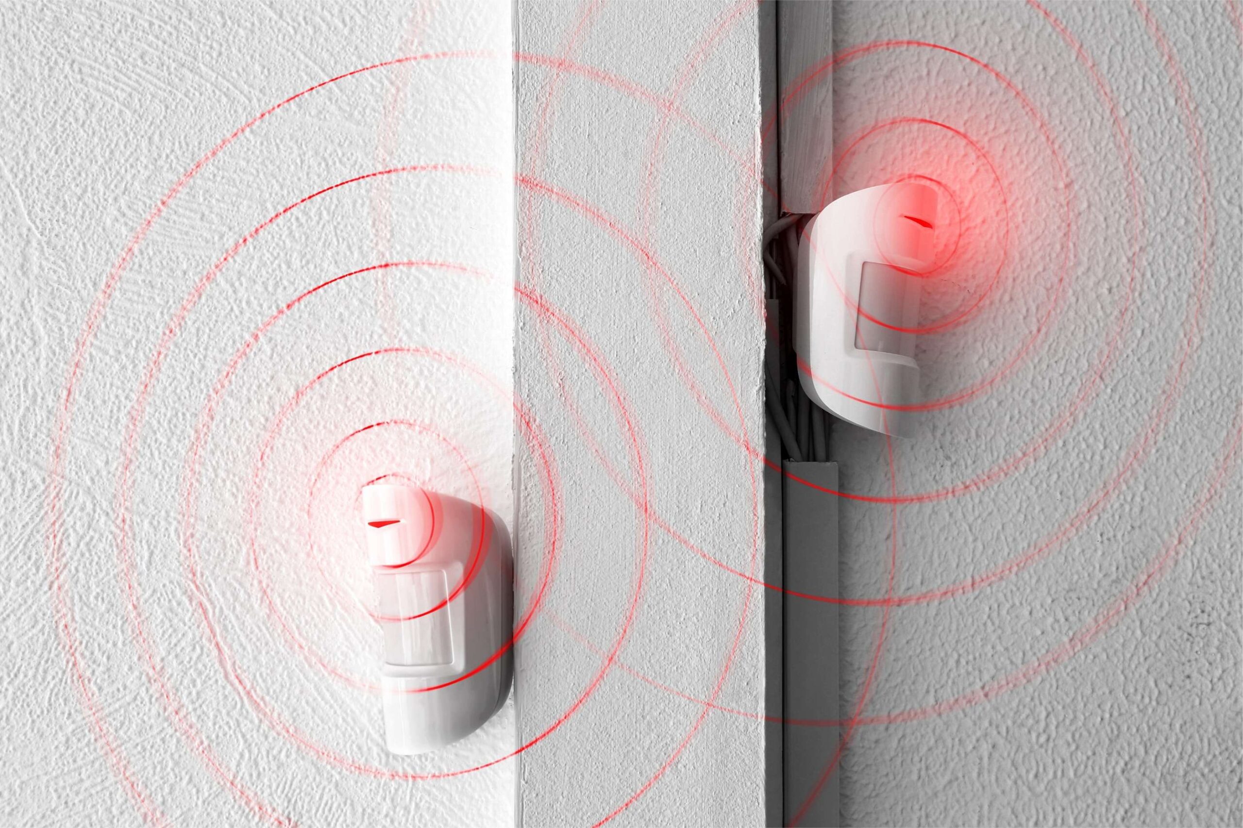 Two white motion detectors mounted on a white wall with red circular graphics representing infrared signal waves for intrusion detection.